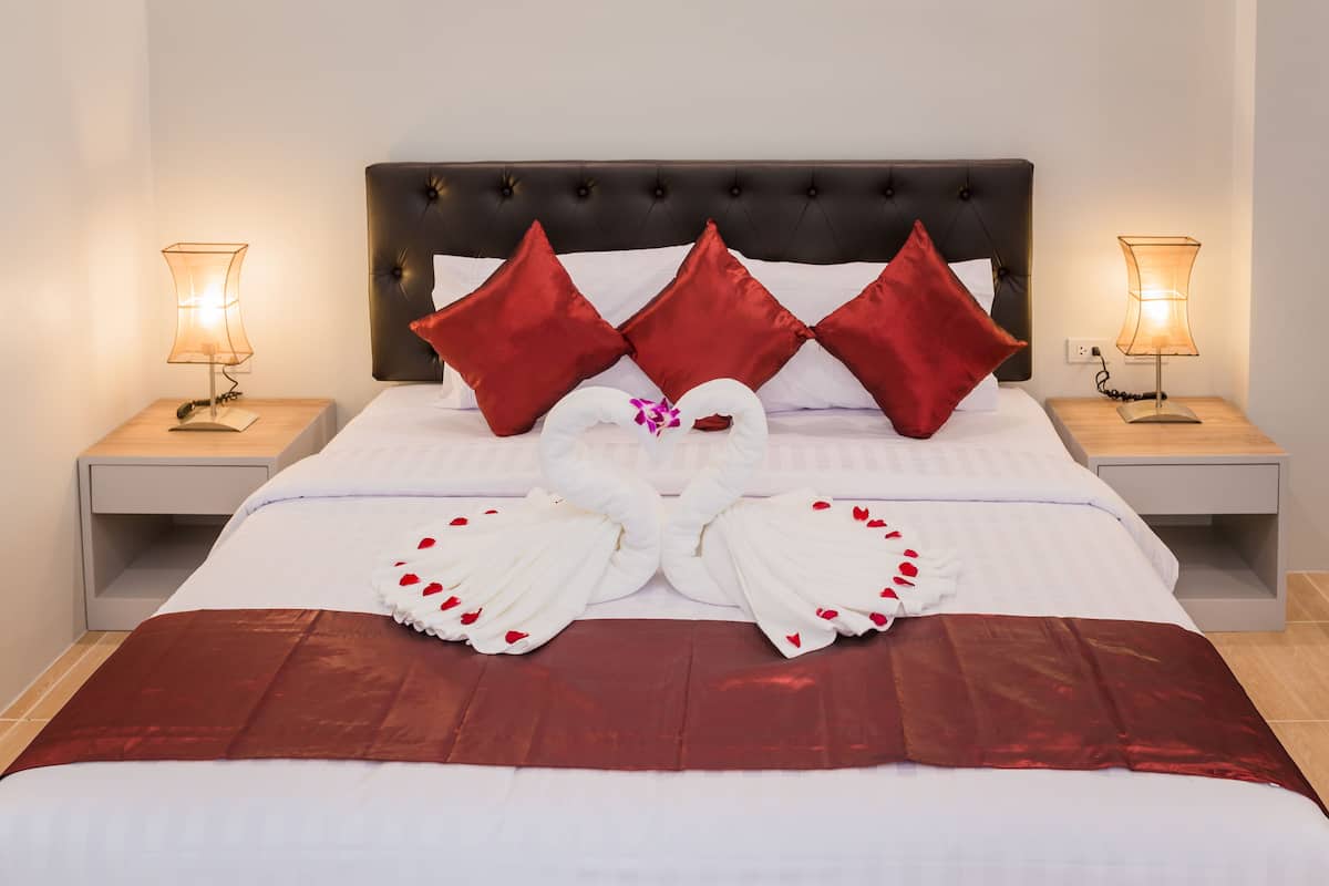 A neatly made bed with a red and white color scheme, two bedside lamps, and a decorative swan pillow arrangement.