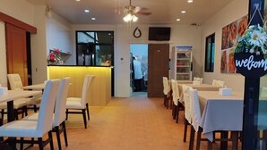A restaurant with a central counter, multiple tables with chairs, and a ceiling fan. - Journey Residence Phuket  (Choeng Thale)