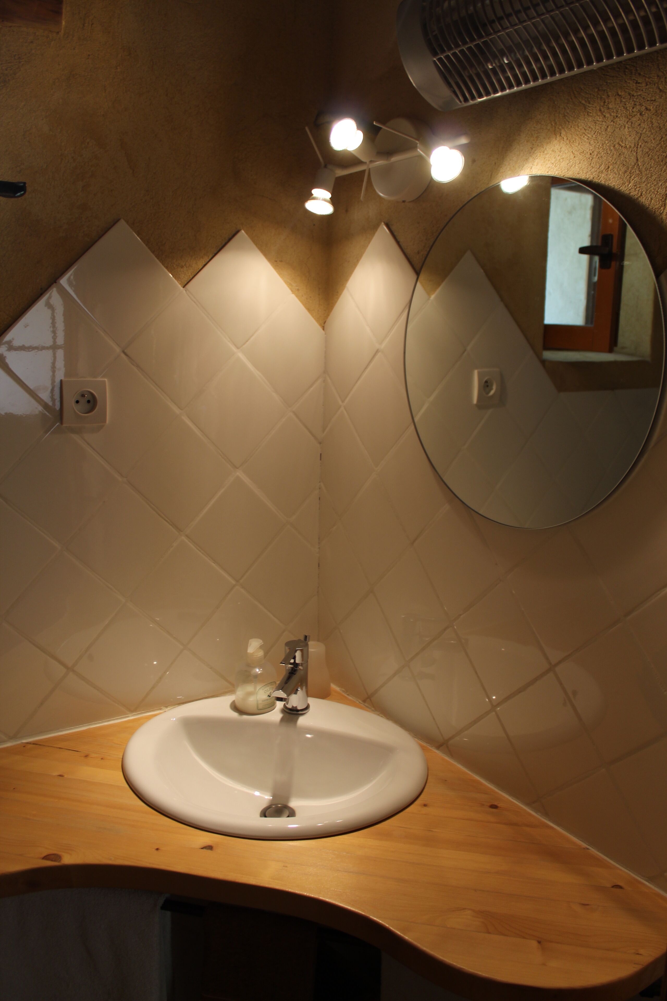 Une salle de bain avec un meuble-lavabo en bois, un miroir rond et un lavabo blanc.