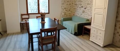 Un comedor con mesa y sillas de madera, ventana con vistas y pared de piedra.