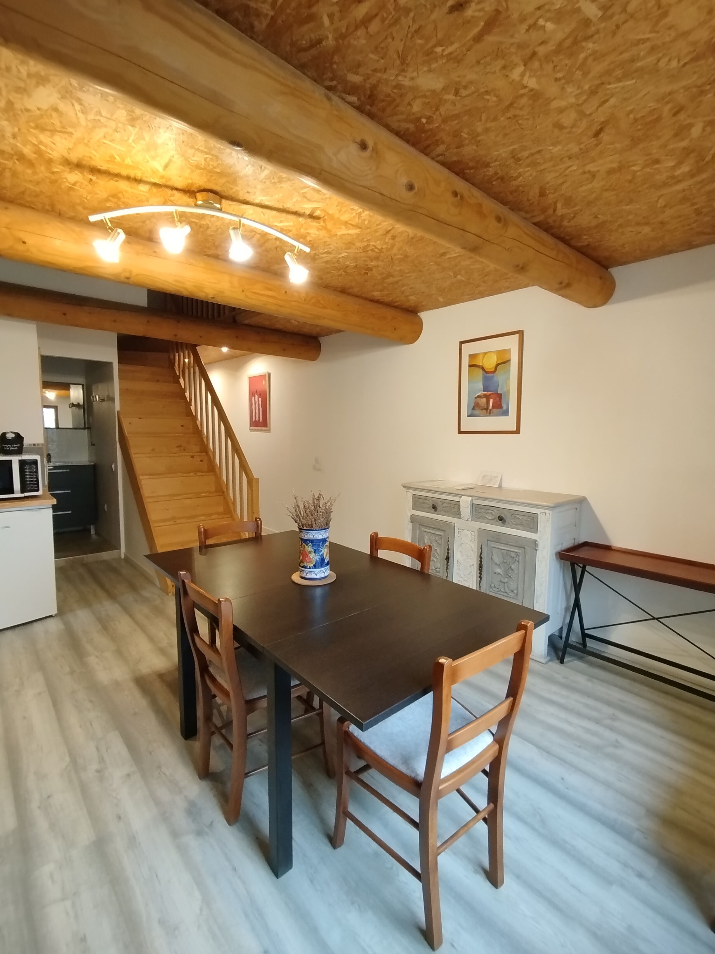 A dining area with a wooden table and chairs, a staircase, and a kitchen in the background.