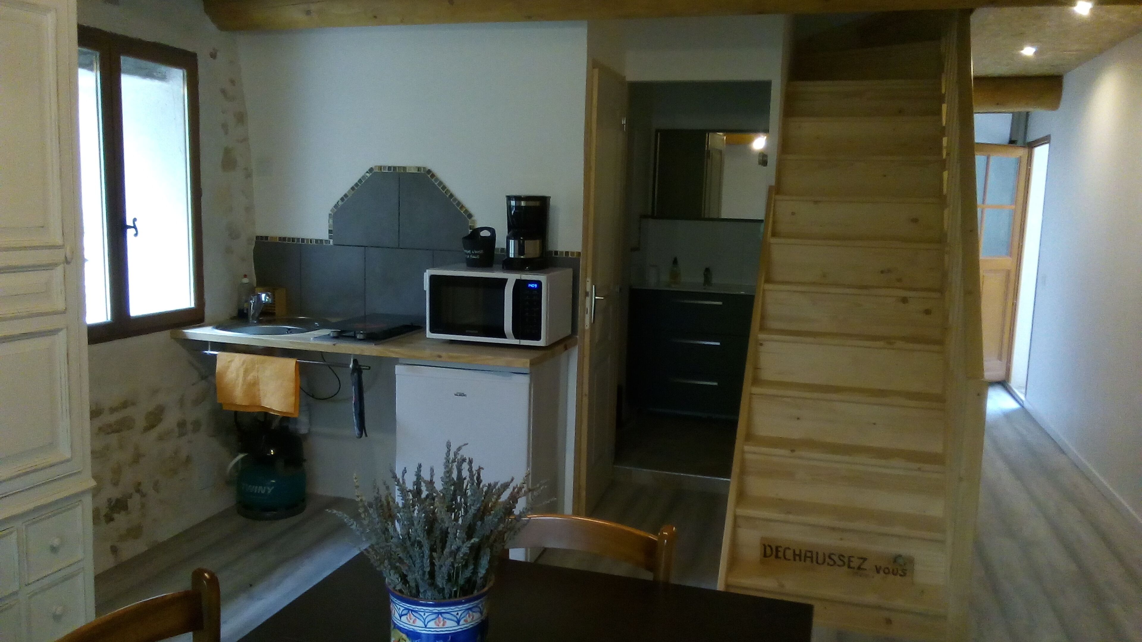 Une cuisine compacte équipée d’un four à micro-ondes, d’un évier et d’un petit réfrigérateur. Un escalier en bois mène à une autre pièce.