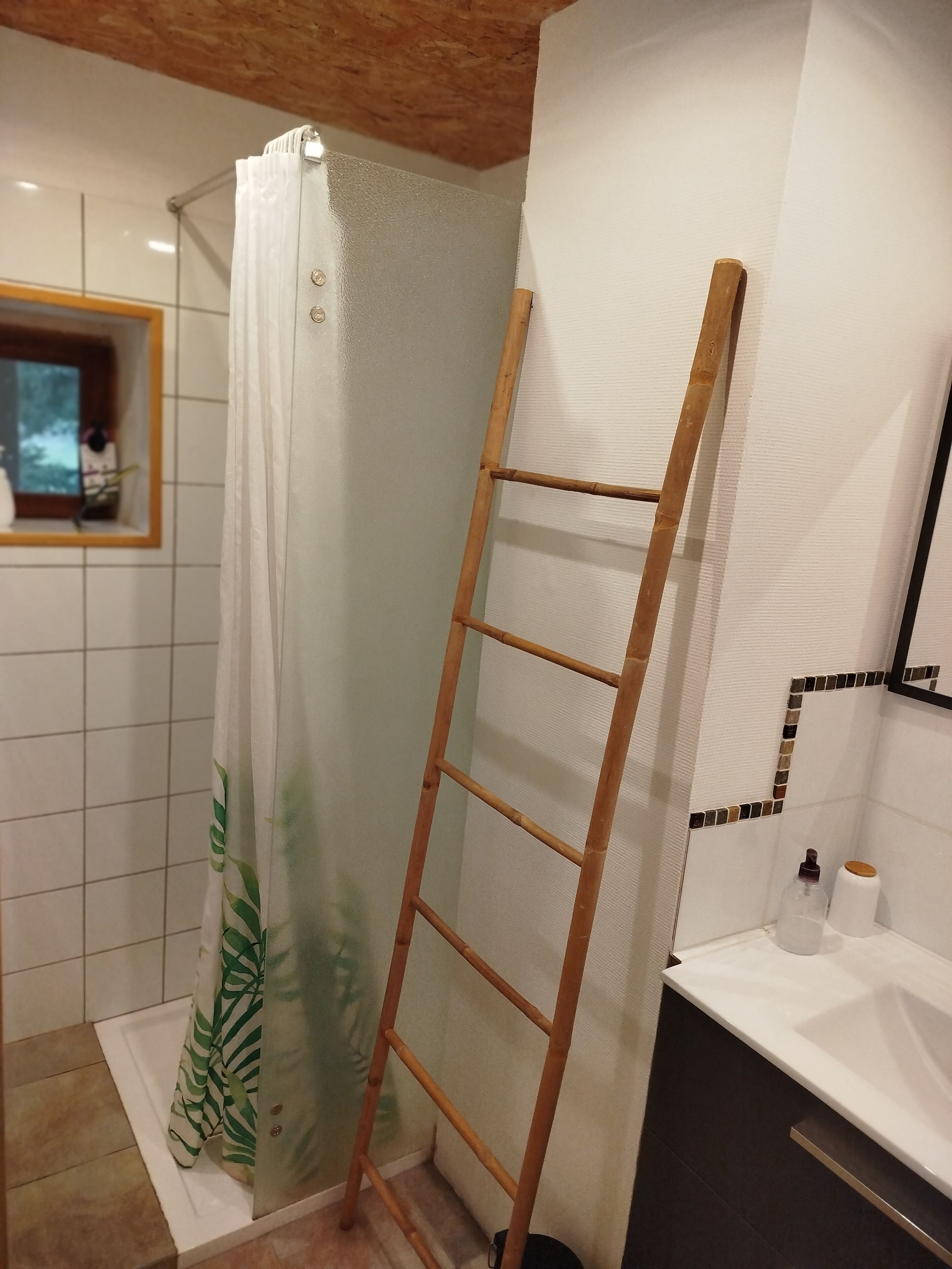 A bathroom with a shower, a wooden ladder, a white sink, and a mirror.