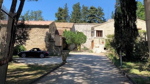 Un edificio de piedra con techo de tejas, un camino de grava que conduce a él, y árboles al fondo.