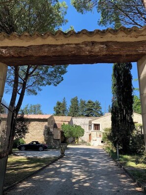 Un edificio de piedra con techo de tejas, un camino de grava que conduce a él, y árboles al fondo.