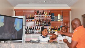 Eine Bar mit einem Fernseher, Regalen voller Spirituosenflaschen und einer Theke, an der eine Person eine Karte aushändigt.