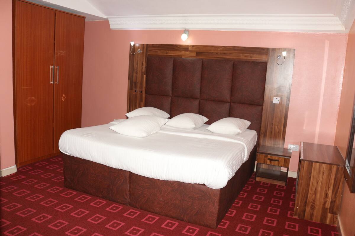 Un dormitorio con una cama grande, un armario de madera y una alfombra roja estampada.