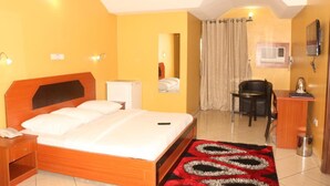 Ein Hotelzimmer mit einem hölzernen Bett, einem Schreibtisch, einem Stuhl, einem kleinen Tisch, einem Spiegel und einem Fernseher.