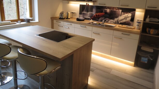 A modern kitchen with a central island, bar stools, a built-in oven, and a window providing natural light. - Domizil Adler (Dresden)