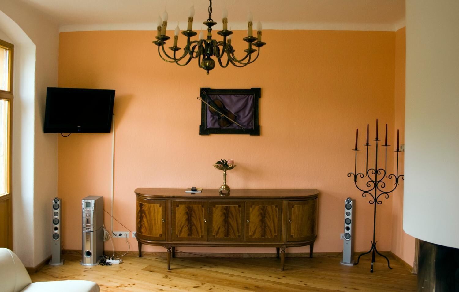 Une pièce dotée d’un plancher en bois, d’un buffet en bois foncé, d’un lustre, d’un téléviseur à écran plat fixé au mur et d’un chandelier.