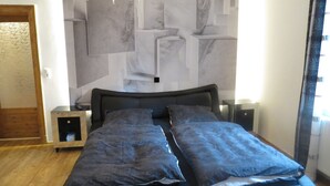 A bedroom with a bed, nightstands, a modern chandelier, and a marble-patterned wall. - Domizil Adler (Dresden)