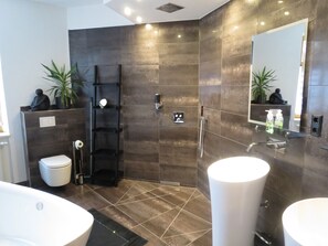 Un baño moderno con ducha a nivel, dos lavamanos y un espejo grande.