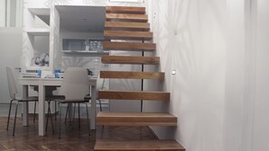 Een modern interieur met een houten trap, een eethoek met stoelen en een tafel, en een keuken met kasten en een magnetron.