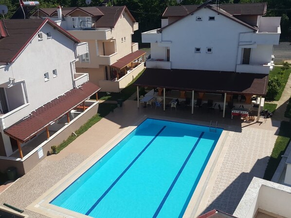 Una piscina con borde de baldosas, rodeada de casas con balcones y un área de patio techada.