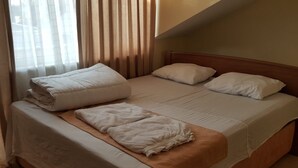 Un lit bien fait, avec des draps blancs et une couverture marron, une tête de lit en bois et une fenêtre avec des rideaux.