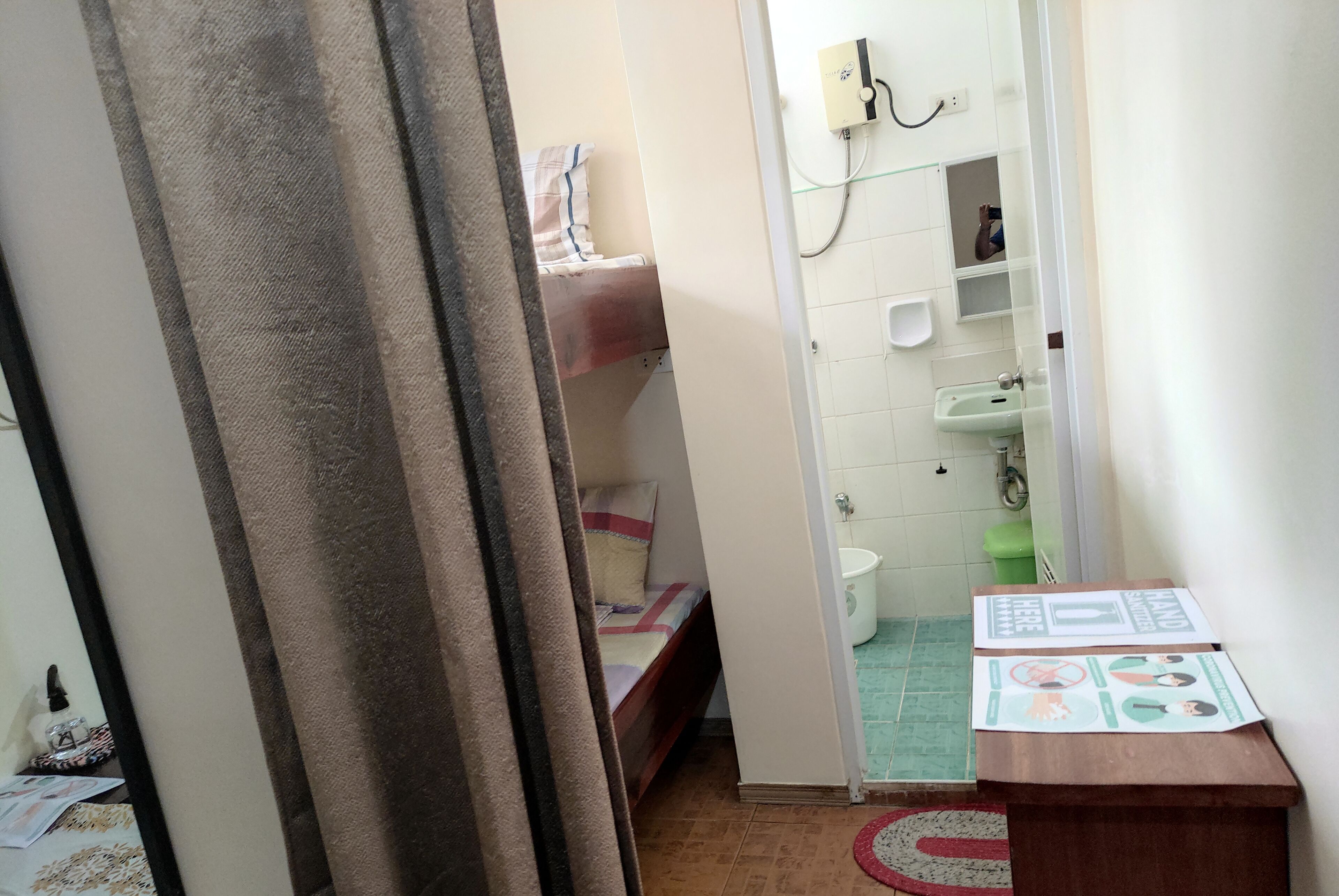 A small, narrow room with a bed, a sink, and a toilet. There is a curtain partially covering the entrance to the room.