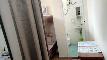 A small, narrow room with a bed, a sink, and a toilet. There is a curtain partially covering the entrance to the room.