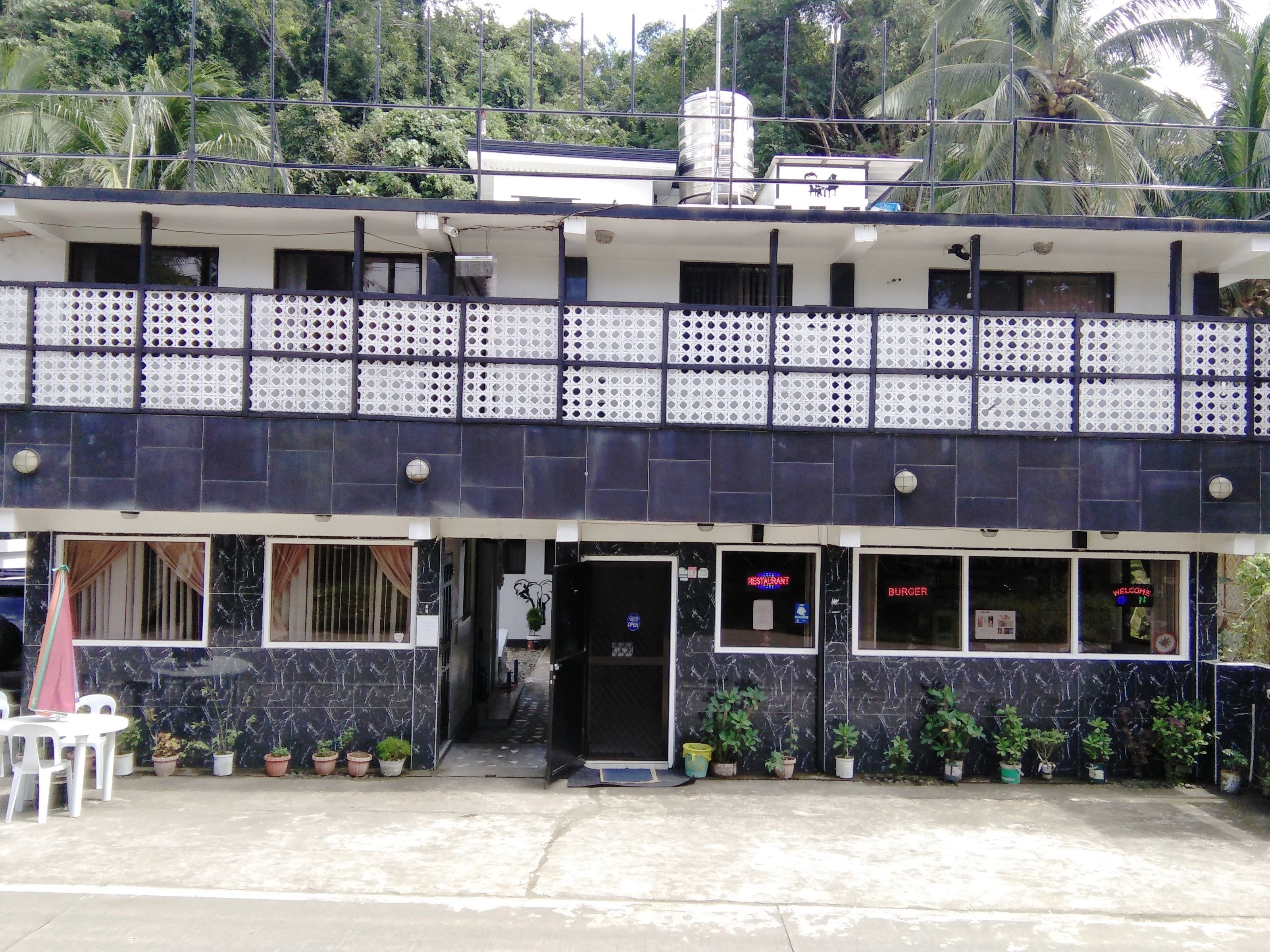 A two-story building with a balcony, potted plants, and a sign indicating a restaurant and burger joint.