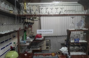 A cluttered bar area with shelves of glasses and bottles, a check-in reception sign, and a calendar on the wall. - Western Highway Lodge (Marabut)
