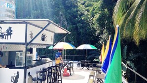 An outdoor seating area with tables and chairs, umbrellas, and a water tank labeled 'FIRST'. - Western Highway Lodge (Marabut)