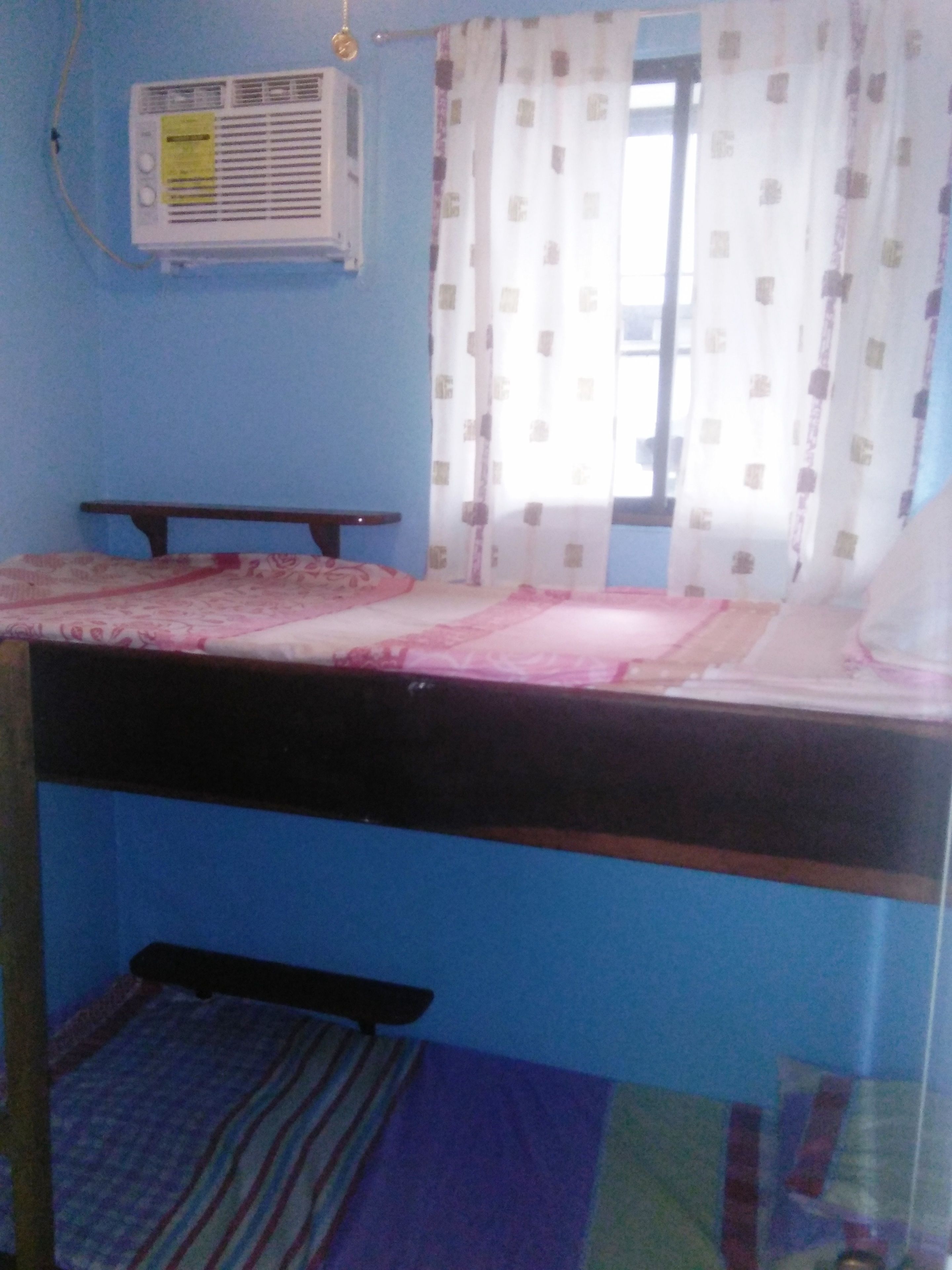 A room with a bunk bed, a small table, and an air conditioning unit on the wall.