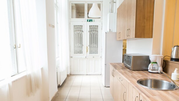 Una cocina con microondas, cafetera y lavabo. Se ve una puerta con una señal de flecha verde.