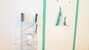 Una estantería blanca con libros y una lámpara, un cuadro con helechos en la pared y detalles pintados en color turquesa.