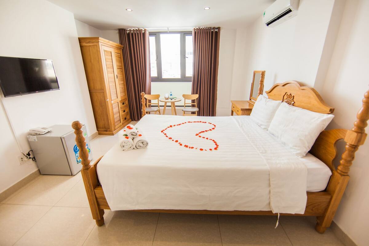 Una habitación de hotel con cama, televisor, armario, escritorio y ventana con cortinas.