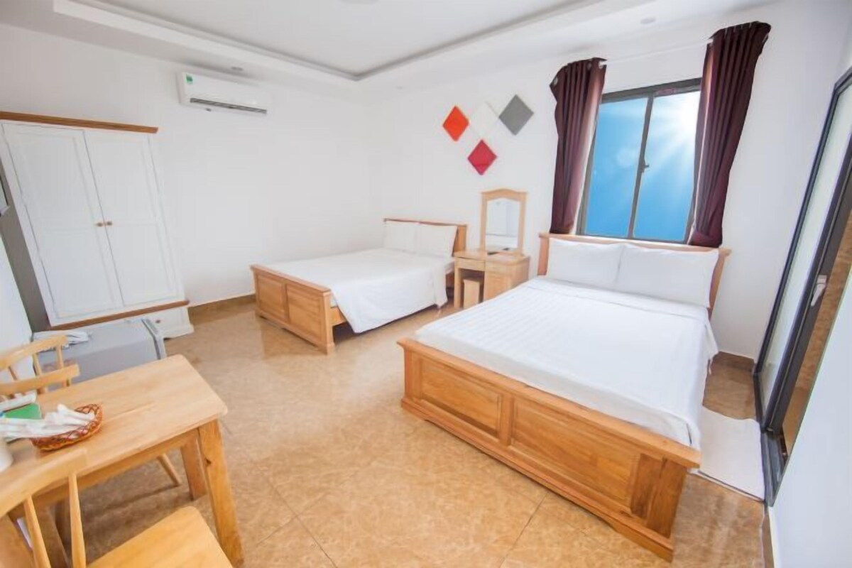 Ein Hotelzimmer mit einem großen Bett, einem kleineren Bett, einem Schreibtisch mit Stuhl, einem Kleiderschrank und einem Fenster mit Vorhängen.