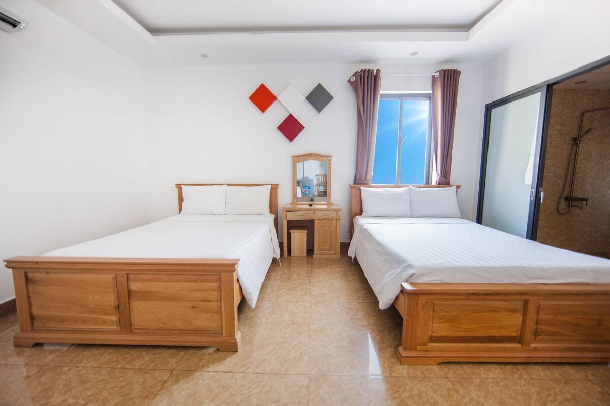 Una habitación de hotel con dos camas de madera, un escritorio pequeño, un espejo y una zona de ducha.