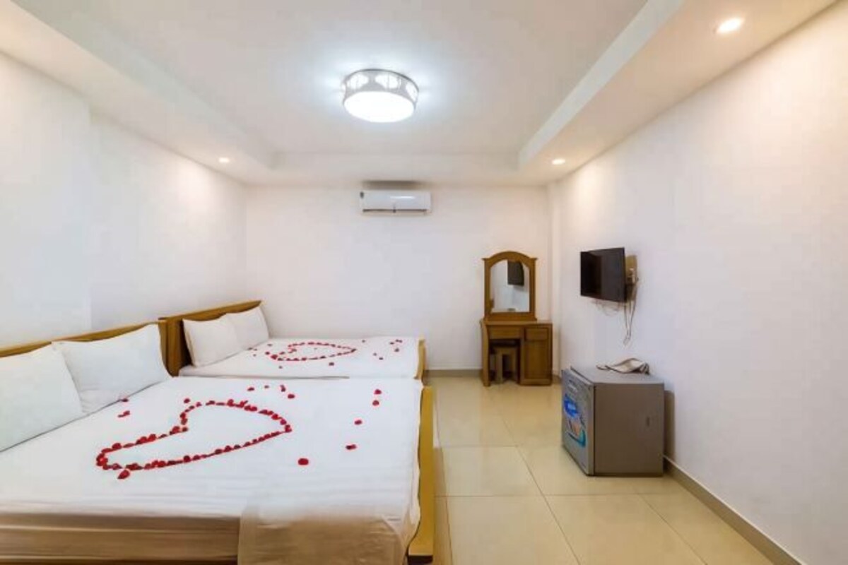 Ein Hotelzimmer mit zwei Betten, einem kleinen Schreibtisch, einem Fernseher und einer Klimaanlage an der Wand.