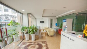 A hotel reception area with a reception desk, seating area, and potted plants.