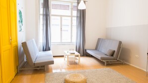 A living room with two sofas, a small table, and a woven ottoman. - Fullhouse Ernesto III (Budapest)