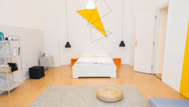 A modern bedroom with a bed, a bookshelf, a small table, and a hanging light fixture. - Fullhouse Ernesto III (Budapest)