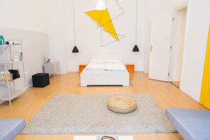 A modern bedroom with a bed, a bookshelf, a small table, and a hanging light fixture. - Fullhouse Ernesto III (Budapest)