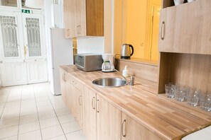 A modern kitchen with wooden cabinets, a stainless steel sink, a coffee maker, and a microwave. - Fullhouse Ernesto III (Budapest)