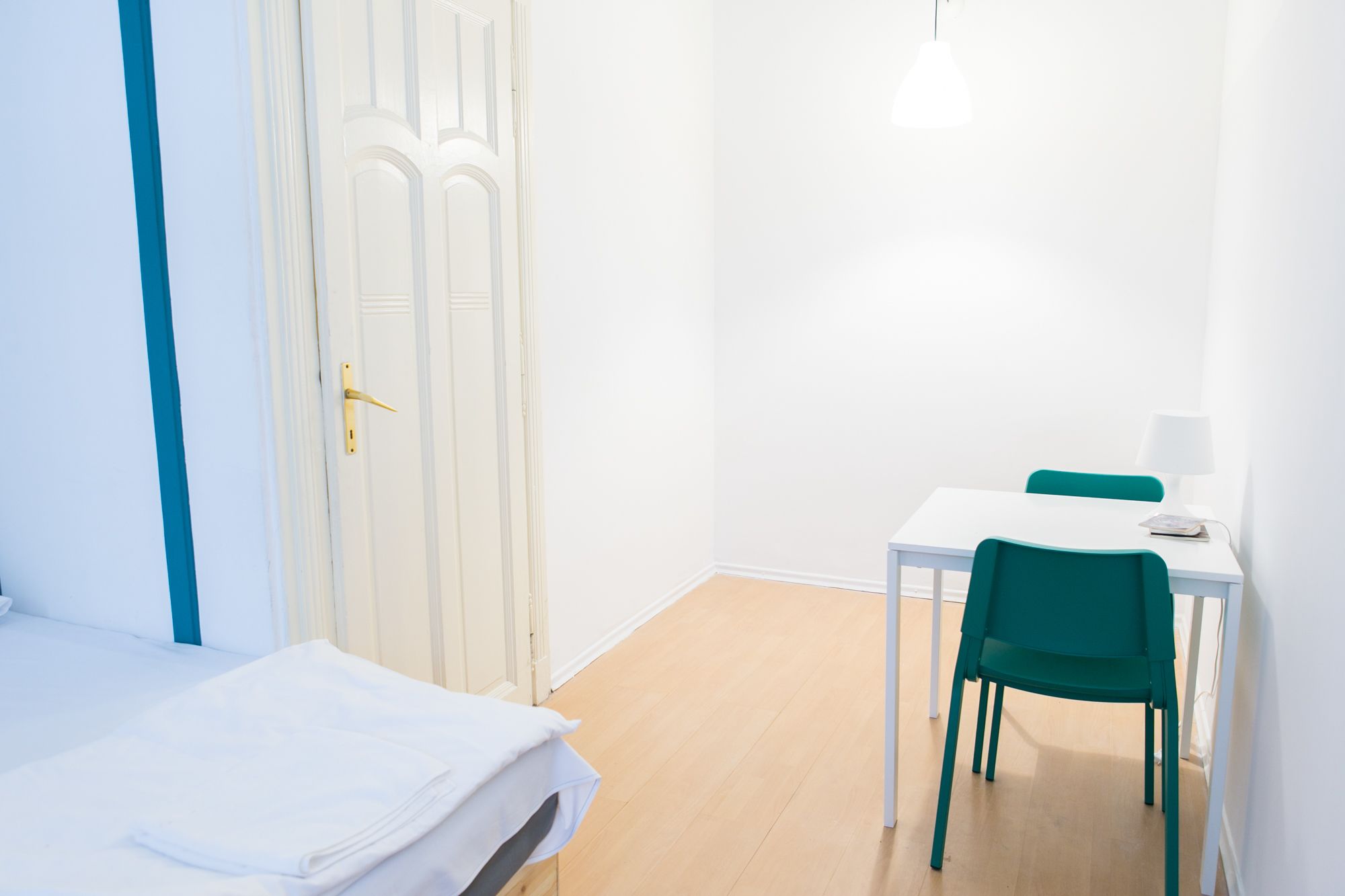 A room with a bed, a desk, a chair, and a hanging light fixture.
