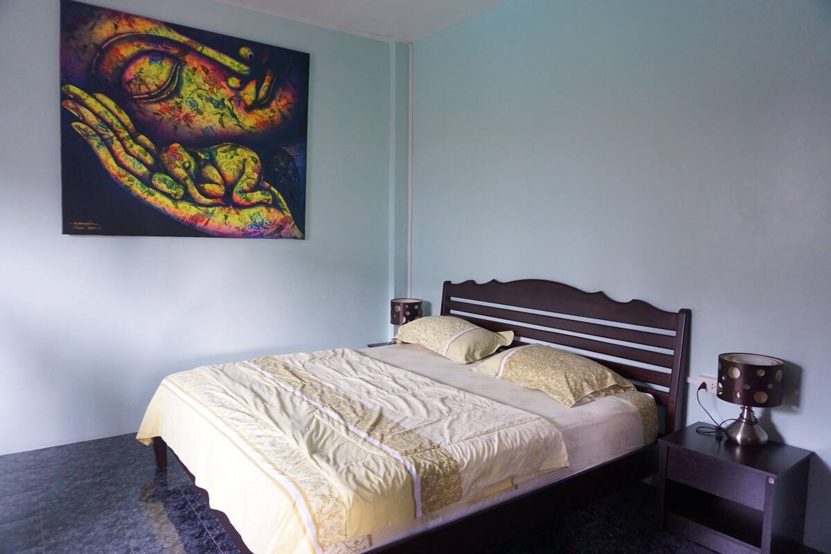 Een slaapkamer met een bed, een nachtkastje, een lamp en een schilderij aan de muur.