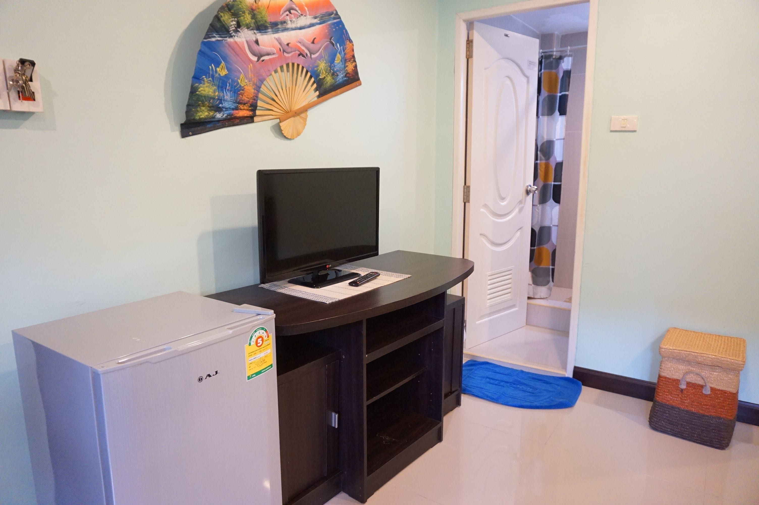 Un ambiente compatto con una TV a schermo piatto su un mobiletto in legno scuro, un piccolo frigorifero e un'opera d'arte colorata appesa alla parete.
