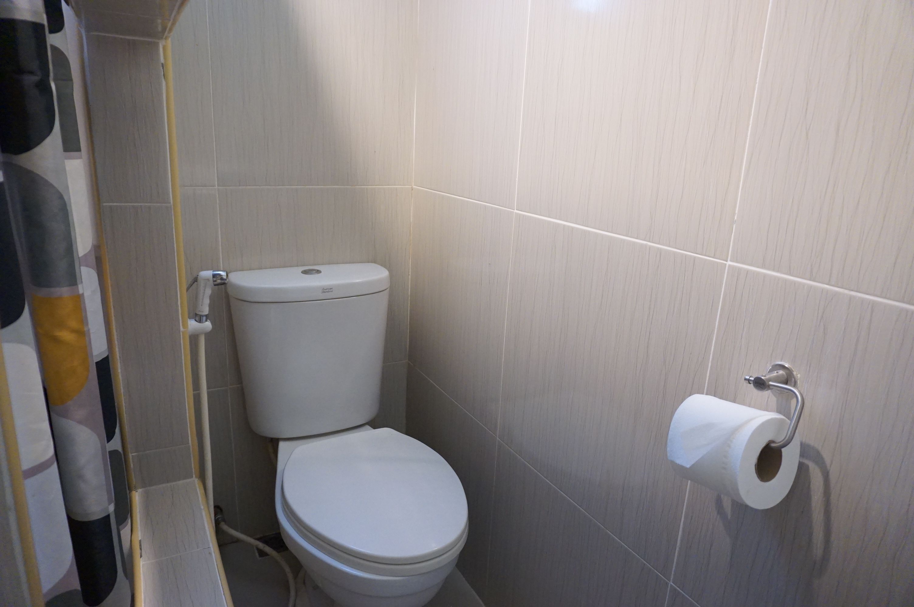 Un bagno con il water, un rotolo di carta igienica a parete e una tenda da doccia.