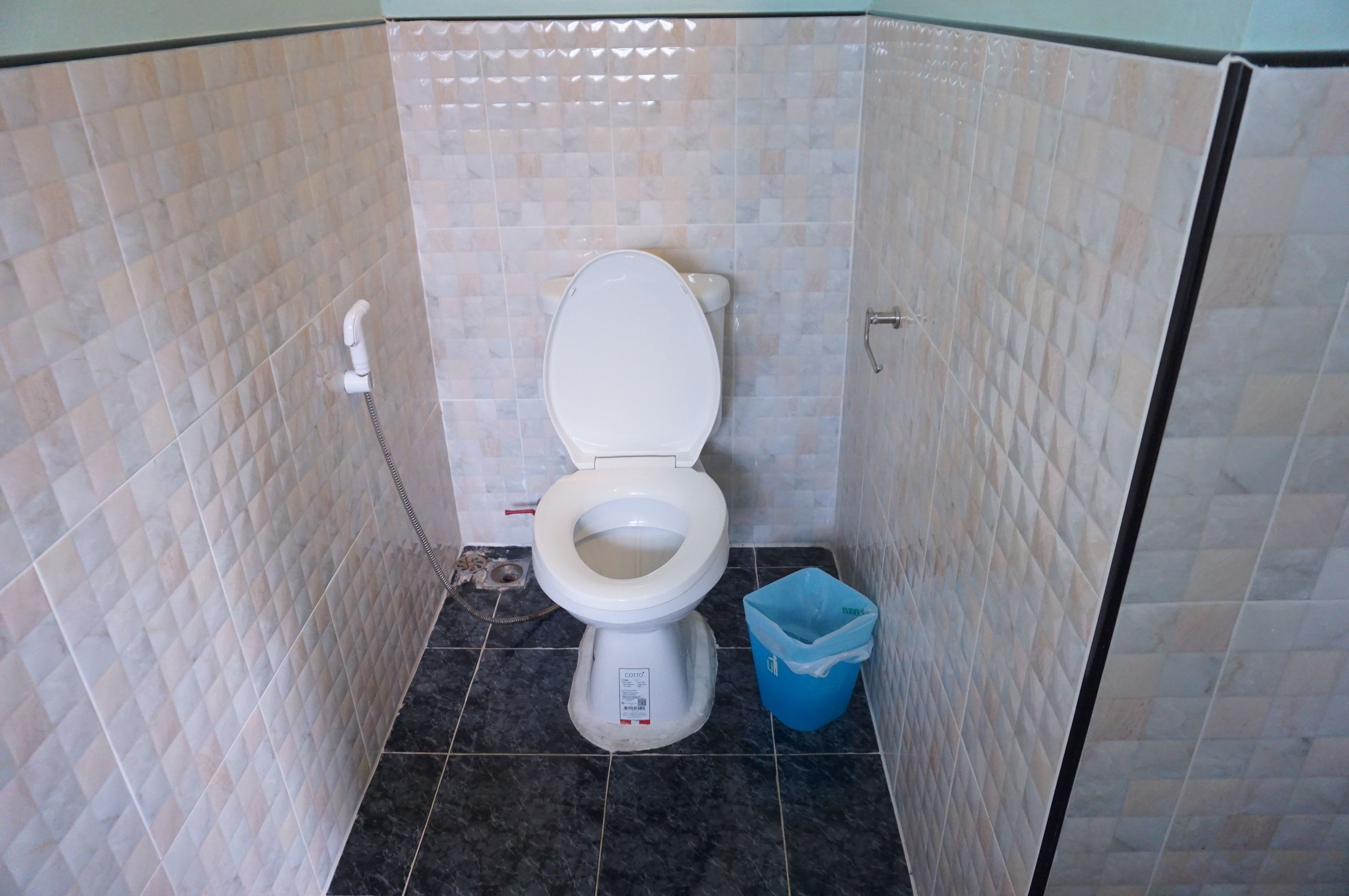 Een kleine badkamer met toilet, prullenbak en betegelde wanden.