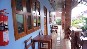 A covered outdoor seating area with wooden tables and chairs, a fire extinguisher, and a view of the surrounding buildings.