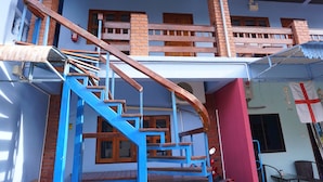 A two-story building with a blue and red exterior, a wooden staircase, and a balcony with a railing.