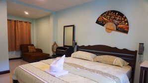 A hotel room with a large bed, a chair, a dresser, a mirror, and a decorative fan on the wall.