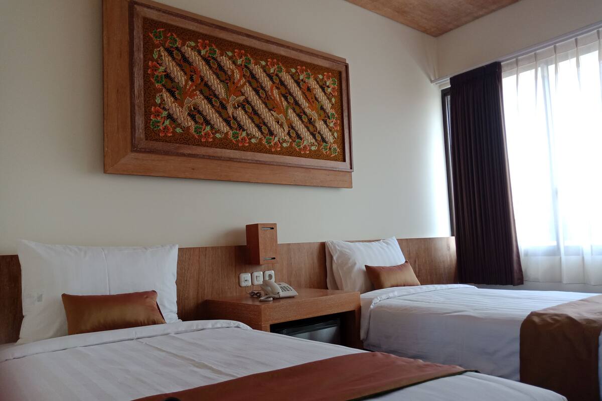 A hotel room with two beds, a wooden headboard, a telephone, and a decorative wall hanging.