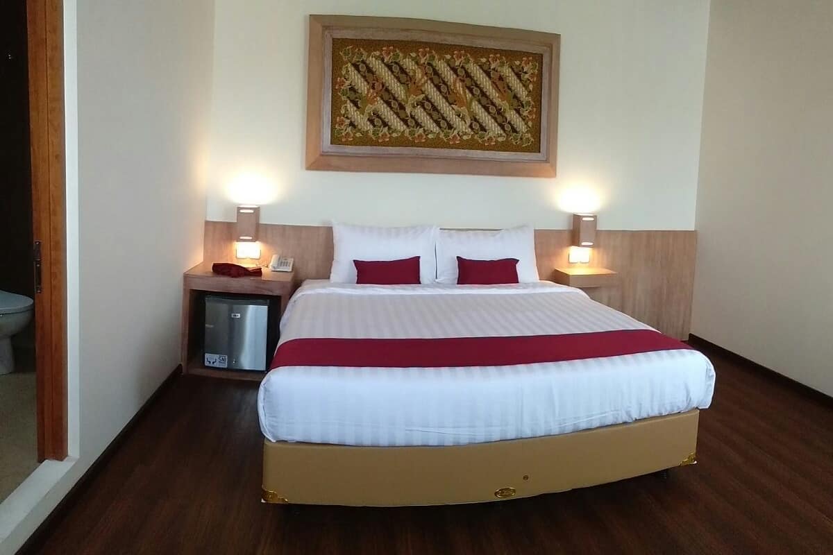 A neatly made bed with white and red bedding, two bedside tables with lamps, and a wooden floor.