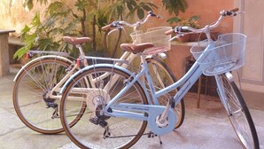 Una bicicleta estacionada en un espacio exterior con piso de piedra y una pared cubierta de plantas trepadoras.