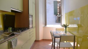Una cocina con comedor, una ventana con contraventanas y vista a la calle.