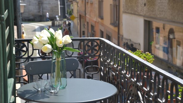 Un balcón con una mesa, sillas y un jarrón de flores blancas.