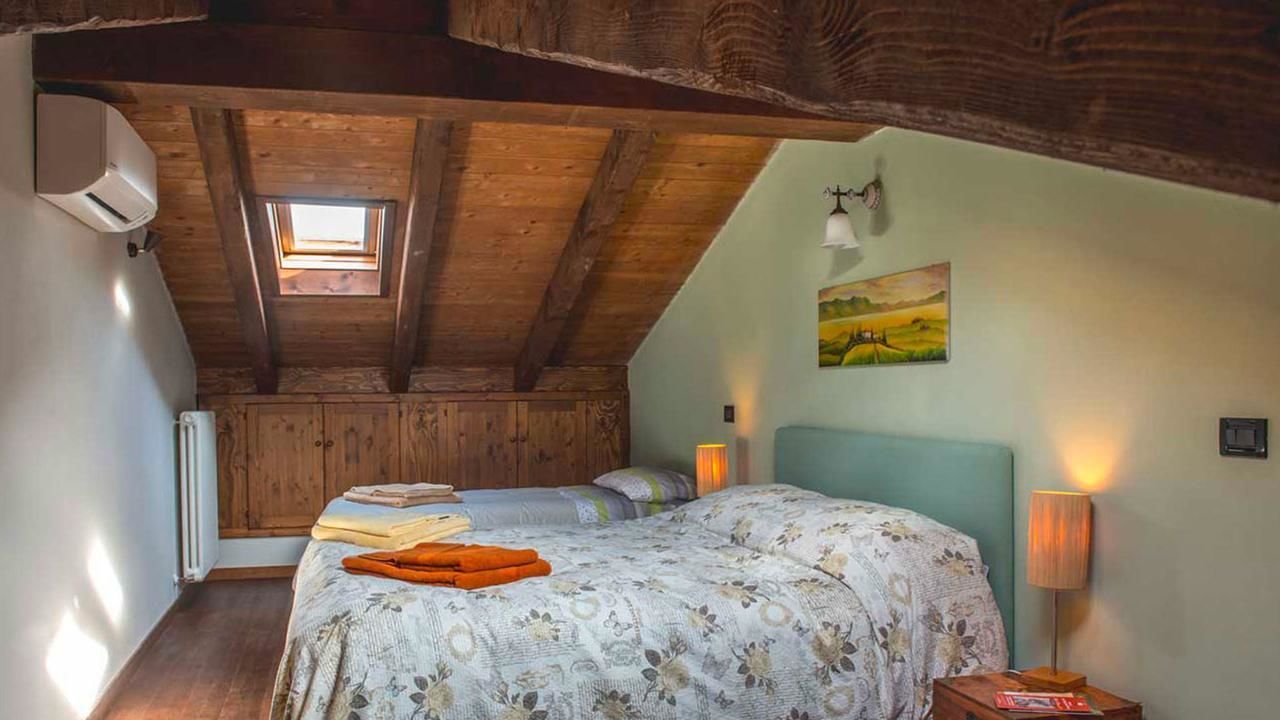 A cozy attic bedroom with a sloped ceiling, a skylight, a bed with floral bedding, a nightstand with a lamp, and a painting on the wall.